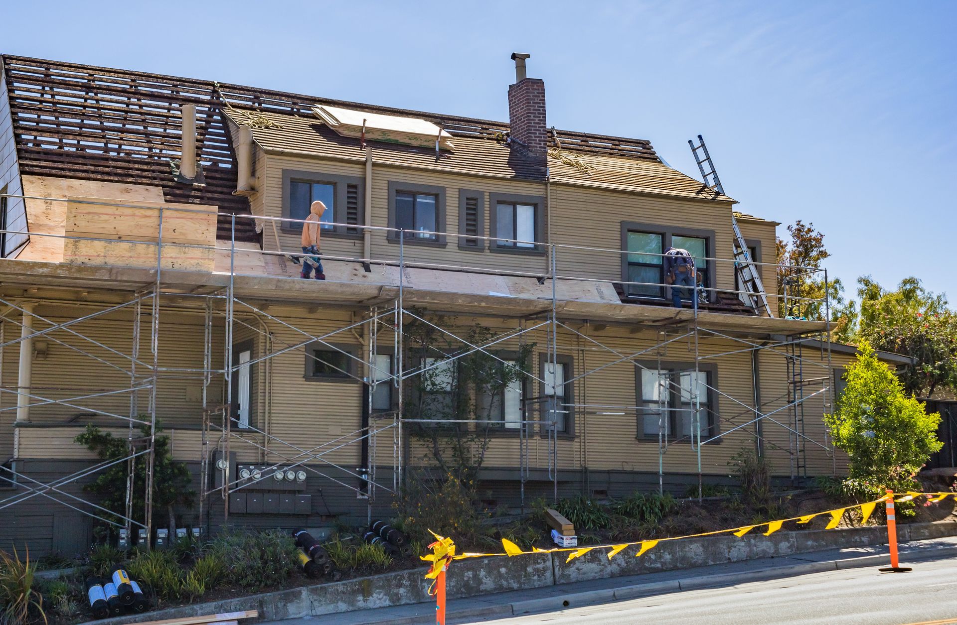 House under renovation with scaffolding and workers fixing the roof on a sunny day.