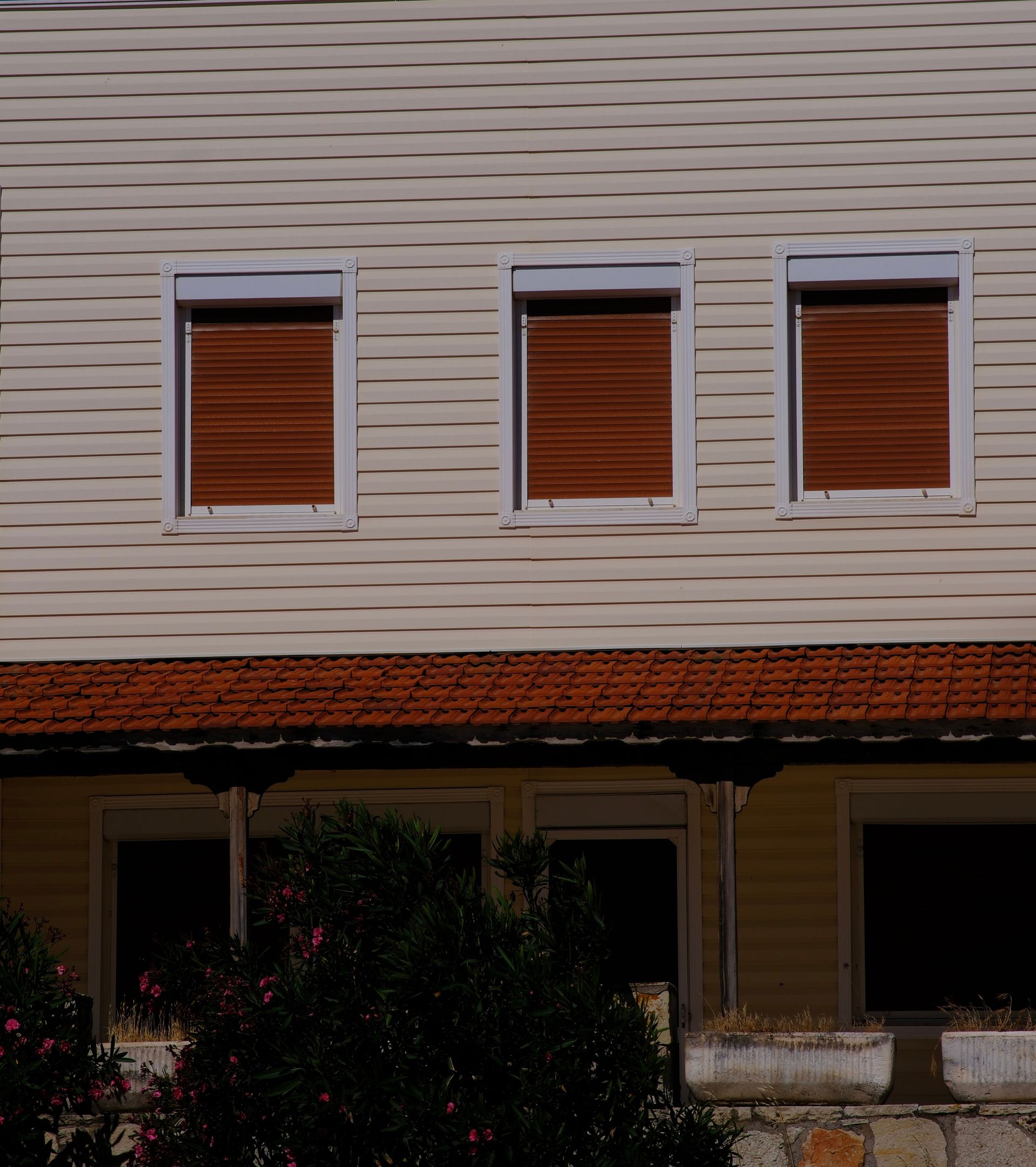 House exterior in Foça, İzmir with closed shutters and tiled roof, photographed in a sunny setting.