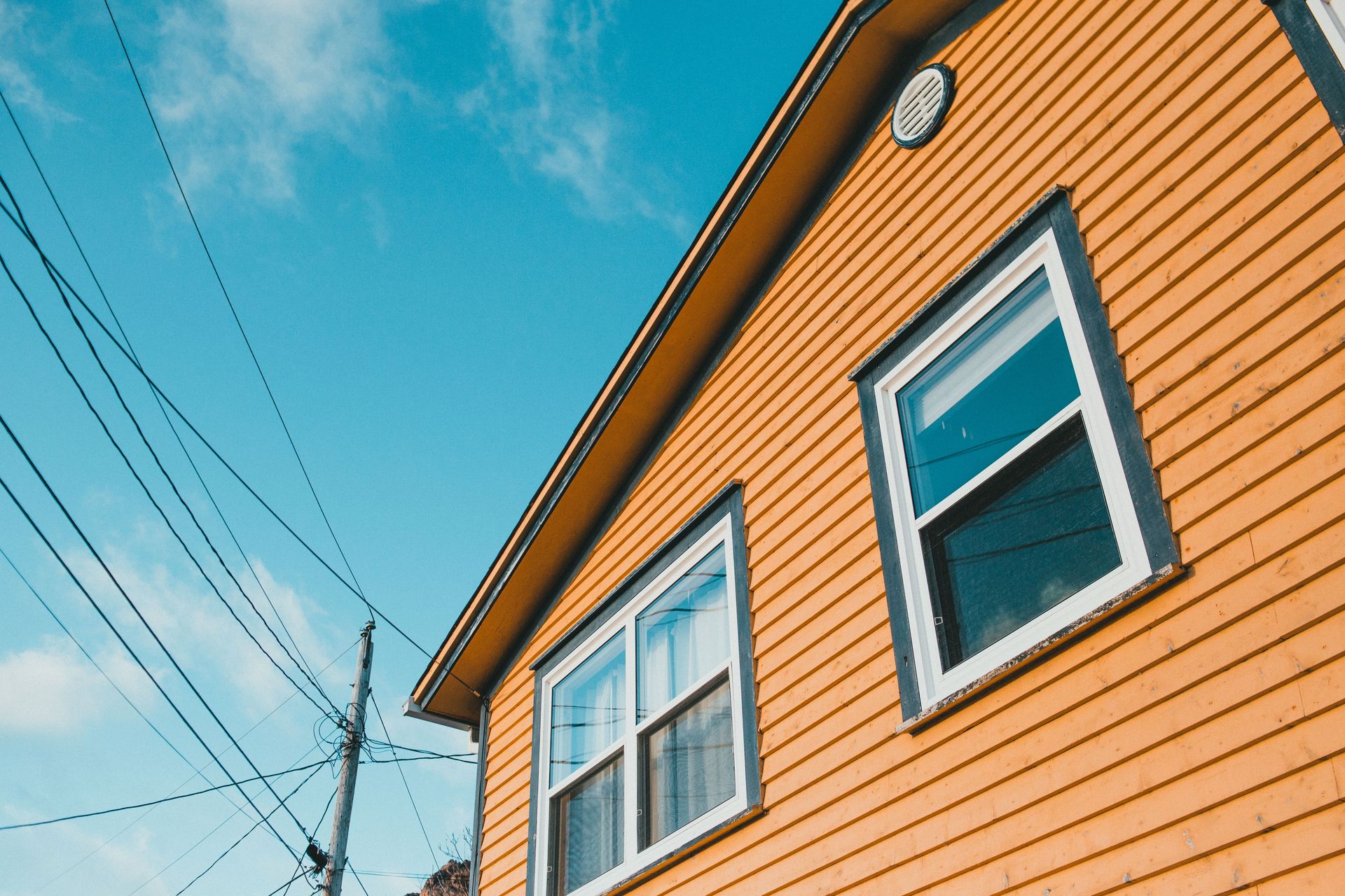 Low-angle shot of a yellow wooden house exterior with power lines against a blue sky.